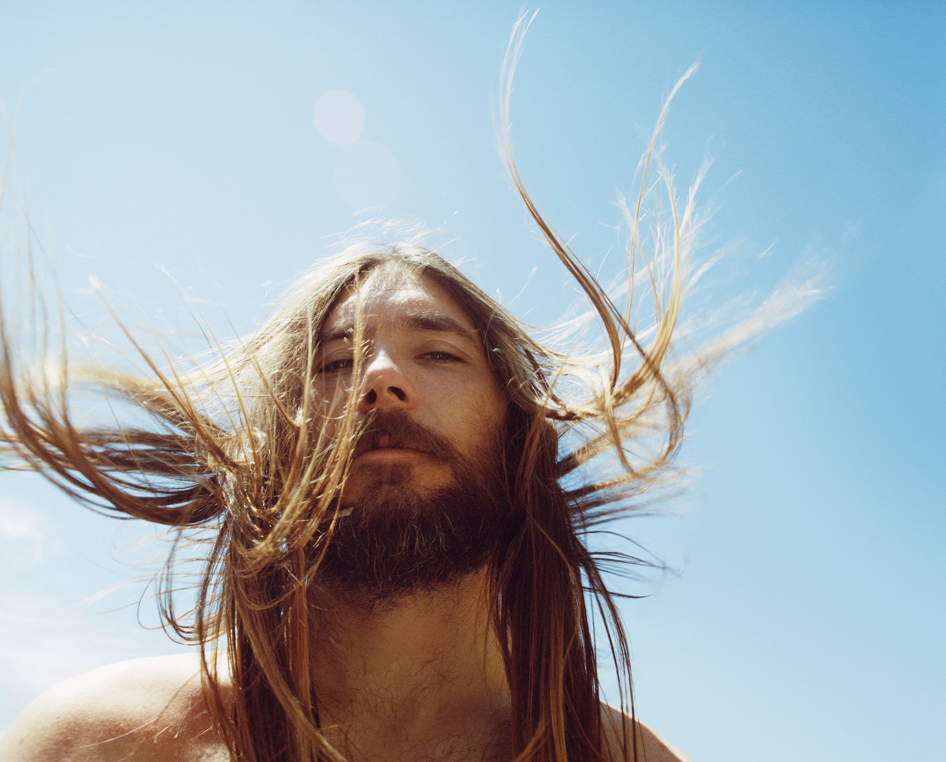 man with hair blowing in the wind, in front of a bright blue sky