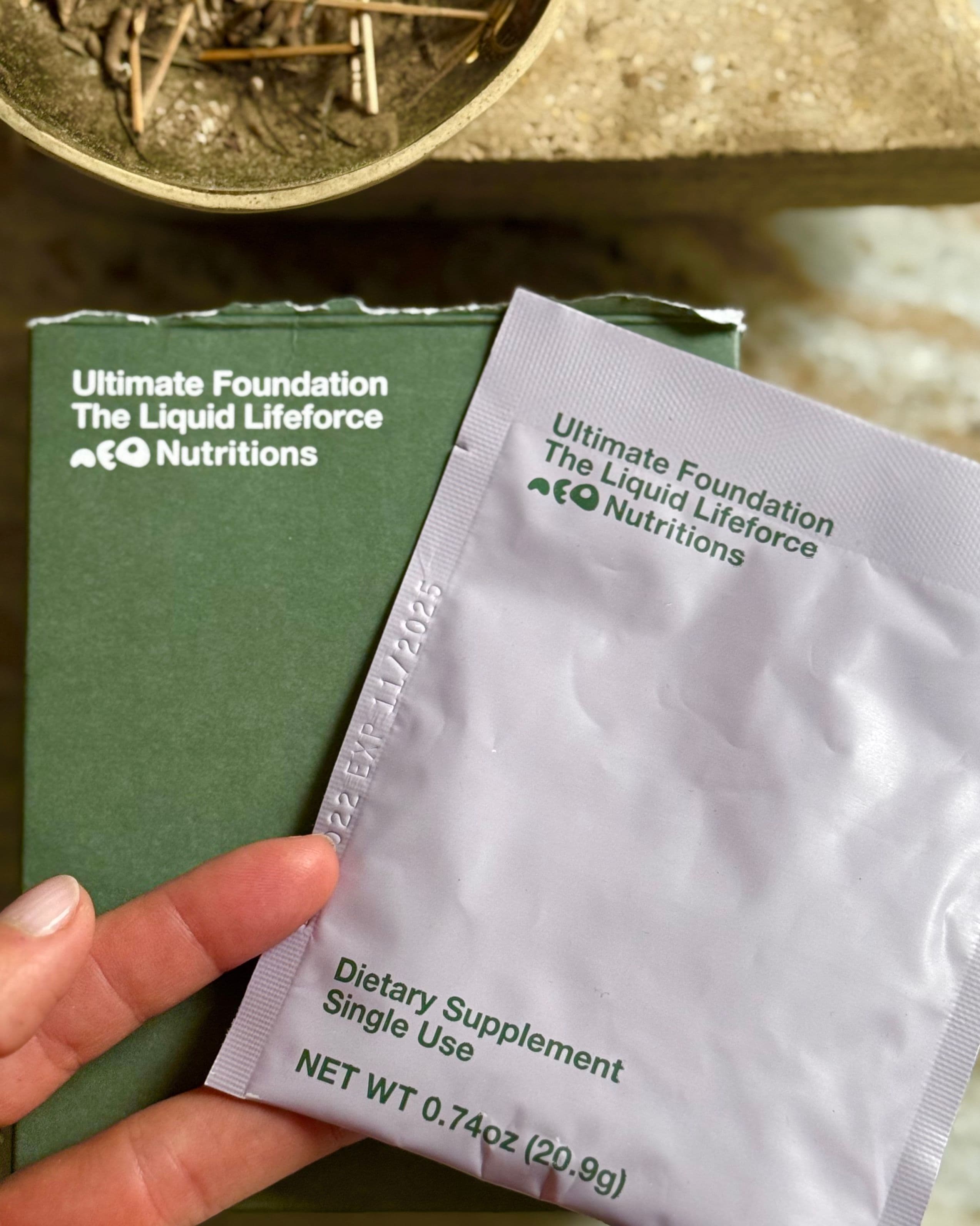 Holding a sachet of Ultimate Foundation next to a bowl of herbs