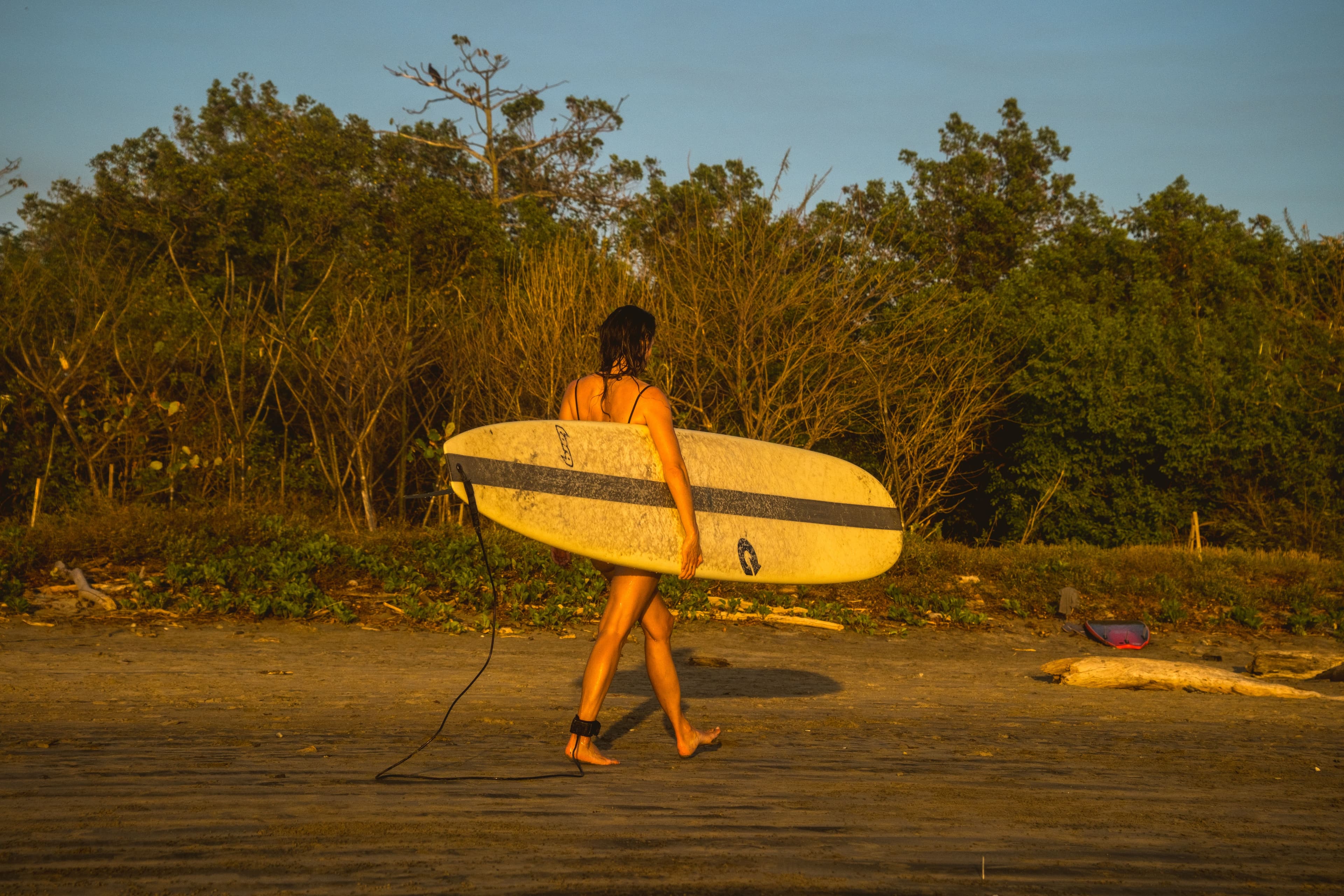 Rachelle Robinett walking on the beach holding a surfboard